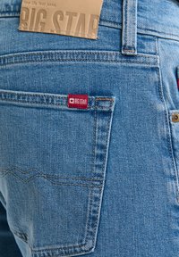 Detailní záběr zadní kapsy modrých džínů z denimu s červenou látkovou značkou Big Star a koženou značkou Big Star na pásku.