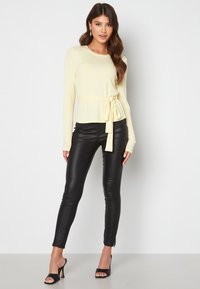 Maglione a coste giallo chiaro con un nodo in vita, abbinato a pantaloni aderenti neri in ecopelle e scarpe con tacco aperte nere.