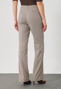 Pantalons taille haute à carreaux en beige et noir, avec une coupe évasée, des poches latérales discrètes et des textures contrastées.