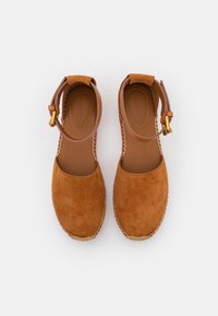 Espadrilles en daim marron avec bout fermé, bride à la cheville et détails en métal doré. Elles comportent une semelle intermédiaire en jute tressé et une doublure intérieure lisse.