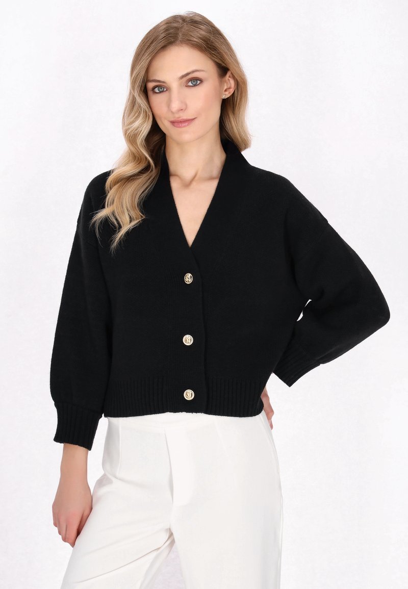 Cardigan corto nero con scollo a V, caratterizzato da quattro bottoni dorati e polsini a coste. Texture in maglia morbida, design svasato e comodo.