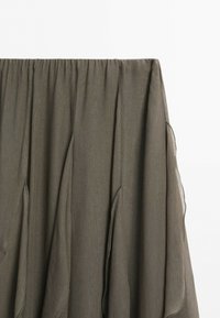 Donkergroene olijfkleurige rok met een geplooide elastische tailleband en gelaagde, vloeiende stofpanelen tegen een effen witte achtergrond.