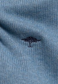 Lichtblauwe gebreide stof met een gladde textuur, met een kleine donkerblauwe boomborduring als opvallend detail.