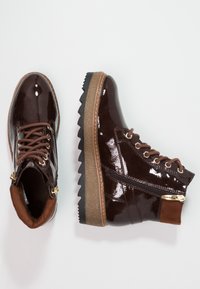 Hnědé lakované kožené kotníkové boty s texturovanou hnědou podešví, se zipem na boku a kontrastními hnědými semišovými akcenty.