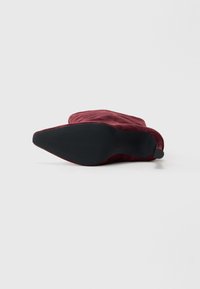 Stivale alla caviglia in suede bordeaux con punta affilata e suola in gomma nera. Presenta un risvolto e una texture liscia.