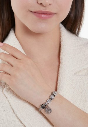 Silver charm bracelet featuring various textured beads, including a tree and elephant design, on a smooth metal chain.