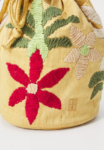 Εμπνευσμένο κίτρινο πουγκί με λουλουδένιο σχέδιο που διαθέτει κόκκινη και πράσινη ραφή. Υφασμάτινη υφή με κλείσιμο τύπου κορδόνι και μικρή λεπτομέρεια επωνυμίας.