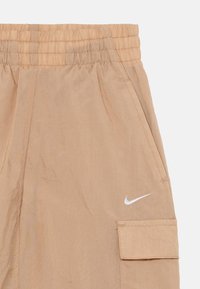 Shorts Nike beige clair avec une ceinture élastique, un tissu texturé et une poche cargo sur le côté avec un accent de logo blanc.