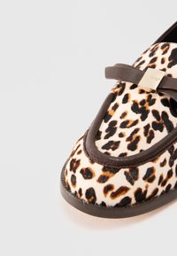 Flat sko med leopardmønster, brun kant og stropp som har en gull firkantet spenne, på hvit bakgrunn.