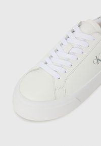 Sneaker bianco in pelle con punta rotonda, lacci piatti bianchi e una tomaia texturizzata. Presenta un logo discreto sul lato e una suola imbottita.