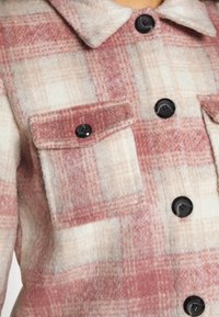 Rød og beige ternet flannel skjorte med sorte knapper, to brystlommer og en blød tekstur med knapkrave.