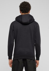 Zwarte hoodie met een grote capuchon, geribbelde manchetten en zoom. Gladde textuur, eenvoudig ontwerp en geen zichtbare patronen of accenten.
