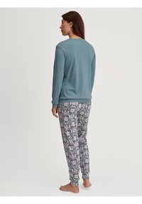 Langsleeve teal top met een ronde hals, gecombineerd met een broek met een patroon van bloemen in roze en groen op een lichte achtergrond.
