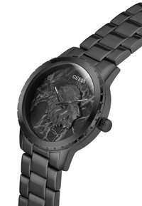 Ceas Guess negru are un emblemă cu un leu pe un cadran marcat întunecat, completat de o brățară metalică neagră elegantă și detalii lucioase.