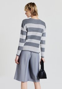 Maglione a righe grigie e bianche in maglia, con maniche lunghe e scollatura rotonda, abbinato a culotte plissettate grigie e una piccola borsa nera.