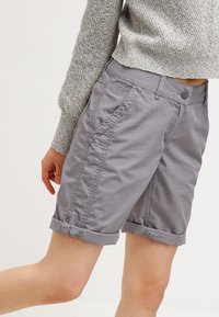 Pantalones cortos de color gris claro, confeccionados en una tela ligera, con puños enrollados, bolsillos frontales y un cierre de botón en la cinturilla.