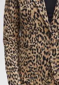 Blazer animalier in tonalità marrone e nera, caratterizzato da chiusura con un solo bottone, rever a punte e tasche laterali con finitura in tessuto testurizzato.