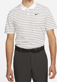 Vit pikétröja med tunna svarta horisontella ränder, en klassisk krage och en svart Nike-logotyp. Kombineras med mörkgrå byxor och ett vävt svart bälte.