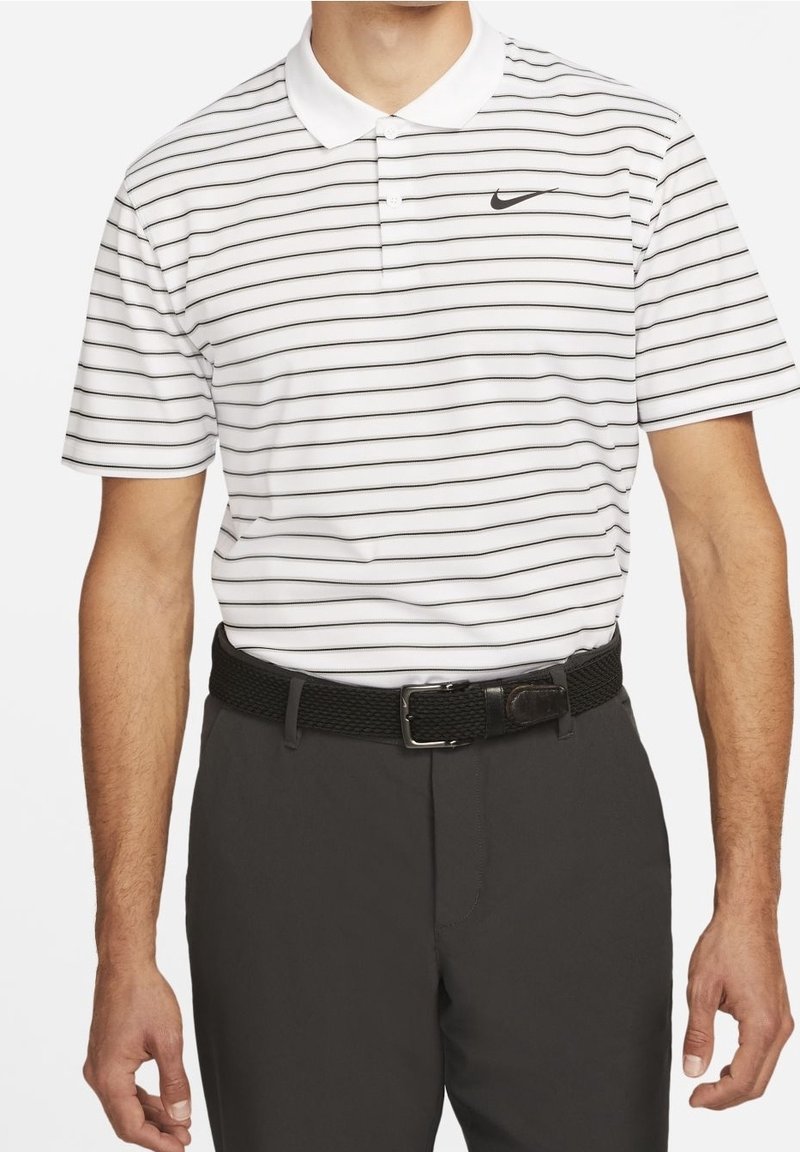 Vit pikétröja med tunna svarta horisontella ränder, en klassisk krage och en svart Nike-logotyp. Kombineras med mörkgrå byxor och ett vävt svart bälte.