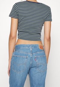 Randig bomullscrop top i grön och marinblå, matchad med högmidjade ljusblå denimjeans med röd etikett och bakfickor.