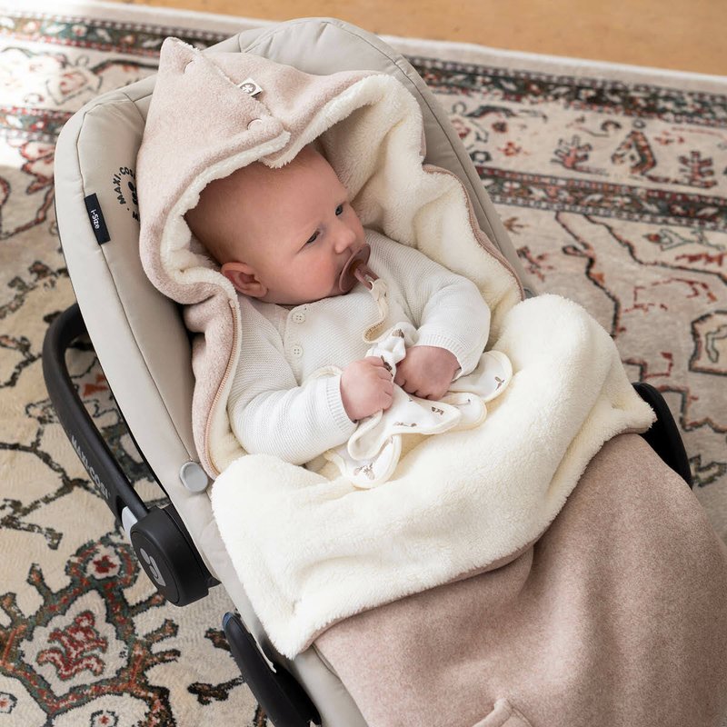 Mjuk beige och krämfärgad babyfilt med huva, som har en texturerad yta och sitter tätt runt ett sittande spädbarn i en gynna.