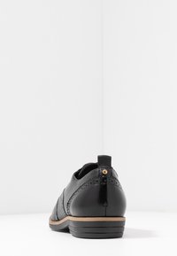 Scarpa in pelle nera con tacco basso, decorazioni brogue e linguetta sul retro. Texture liscia con suola contrapposta color tan.
