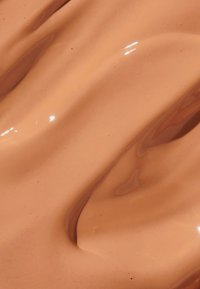 Romige, matte perzikkleurige substantie met een gladde, golvende textuur en een lichte glans. Fijne deeltjes zichtbaar op het oppervlak.