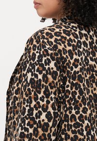 Veste en imprimé léopard avec un tissu texturé présentant des taches noires, brunes et beiges. Le design est ample avec un léger éclat.