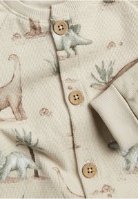 Beige gebreide stof met dinosaurusschema's in zachte kleuren, voorzien van drie houten knopen en een geribbelde manchetrand.