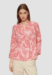 Roze blouse met een patroon, v-hals, lange mouwen en een lichte stof met abstracte ontwerpen in rode en witte tinten.