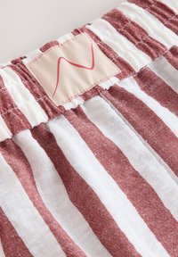 Gros plan d'une ceinture élastique rayée rouge et blanche avec une étiquette beige cousue présentant un simple motif ondulé rouge.