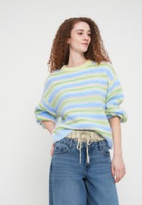 Ριγέ πουλόβερ σε παστέλ αποχρώσεις του μπλε, πράσινου και κρεμ, με στρογγυλή λαιμόκοψη και άνετη γραμμή. Φορεμένο πάνω από καρό πουκάμισο, σετ με ανοιχτόχρωμο τζιν.