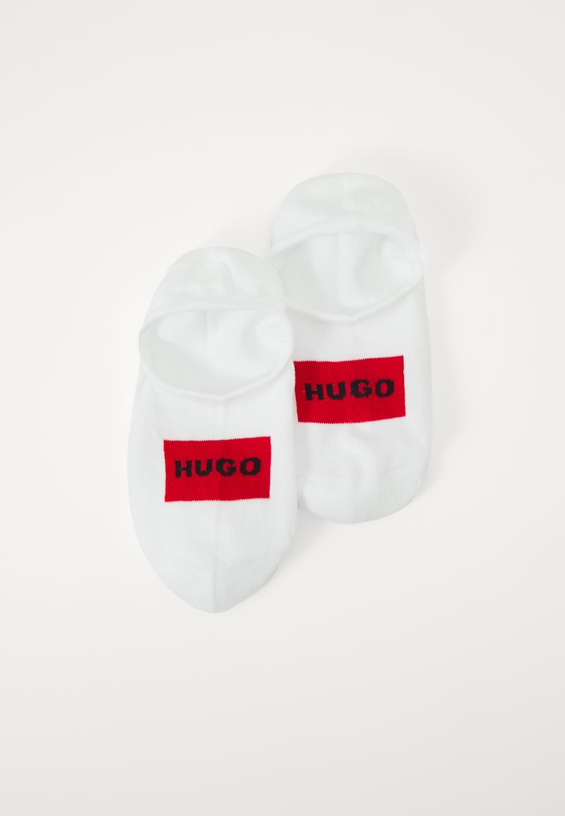 Fehér bokazokni, piros téglalap alakú logóval, amelyen a "HUGO" felirat feketén szerepel. A zoknik sima tapintásúak és lekerekített szélekkel rendelkeznek.