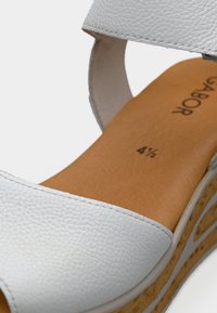 Άσπρο πλατφόρμα σανδάλι με υφή στην επάνω επιφάνεια, ανοικτή μύτη και σόλα που μοιάζει με φελλό. Περιλαμβάνει ορατό όνομα μάρκας και ενδείξεις μεγέθους.