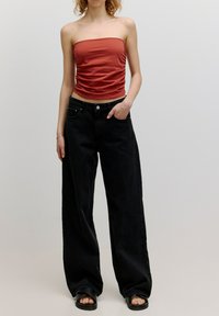 Schwarze weite Jeans mit hoher Taille, kombiniert mit einem figurbetonten roten trägerlosen Oberteil. Weicher Stoff; das Oberteil hat eine geraffte Detailung in der Mitte.