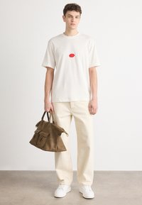 Cremefarvet bomulds T-shirt med en rød oval grafik, parret med lysfarvede bukser og en brun ruskinds håndtaske med struktureret design.
