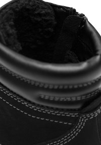 Fekete bőr bokacsizma puha béléssel, varrott díszítéssel és cipzáros záródással. Sima felület kerek nyakrésszel és megerősített peremmel.