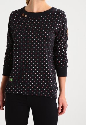Suéter negro de manga larga con un patrón de lunares en rosa y blanco. Presenta un cuello redondo y botones en el hombro; etiqueta verde en el dobladillo.