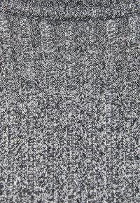 Pull en tricot avec une texture côtelée présentant un schéma de couleurs noir et blanc, mettant en valeur des lignes verticales alternées et des détails fins.