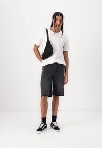 Black denim shorts with frayed hem, white short-sleeve henley shirt, black sling bag, black socks, and black sneakers with white accents.