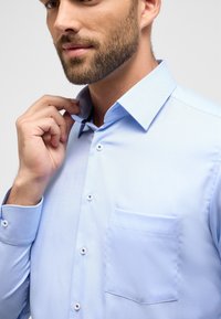 Lichtblauw op maat gemaakt shirt met een klassieke kraag, borstzak en knopenlijst. Heeft een textiele stof met een subtiel diagonaal patroon.