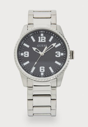 Montre en acier inoxydable argenté avec un cadran noir, de grands index horaires numériques et un bracelet en maillons argentés. Présente une lunette texturée.