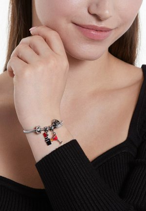 Silver charm bracelet featuring colorful charms: a black dress, a cocktail glass, and a small accessory. Worn on a bare wrist, with black clothing.