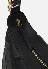 Black leather handbag with a quilted texture, gold-tone zipper, and hardware. Features a flat strap with a smooth finish and detailed stitching.