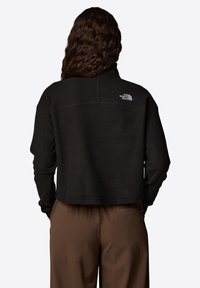 Czarna, krótka bluza z długimi rękawami, z wysokim kołnierzem i logo na górnej części pleców. Gładka tekstura i luźny krój.