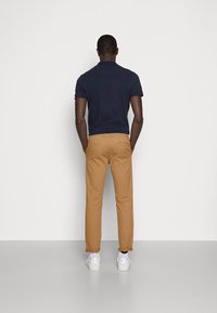 Marinblå polo shirt, khakifärgade byxor, vita sneakers. Klädseln har en figursydd design, synlig sömnad och uppvikta byxben.