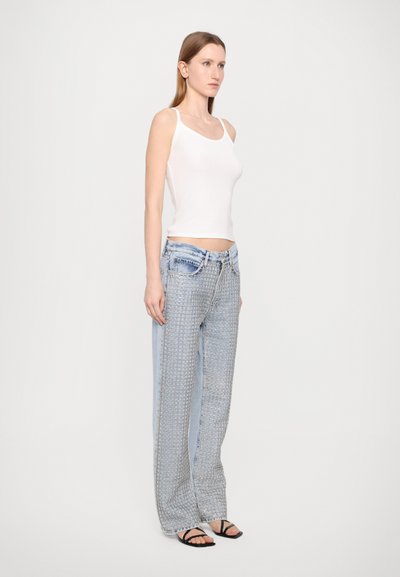 White fitted tank top paired with light blue patterned wide-leg jeans, featuring a mix of denim textures and a front fastening. Black sandals.