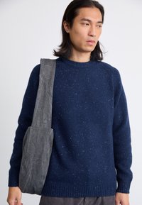 Marineblauwe gebreide trui met een ronde hals en gemêleerde structuur, gecombineerd met een grijze stoffen schoudertas met een brede schouderband.