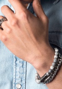Silver and beaded bracelets on a hand, featuring round, marbled beads and a chain link design, with a textured denim background.