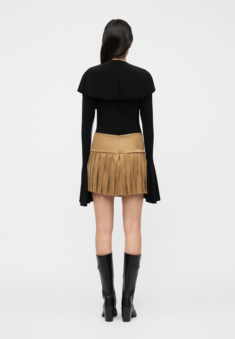Haut noir avec un col en forme de cape, associé à une jupe marron clair à franges. Bottes noires montantes complètent le look. Design et couleurs minimalistes.